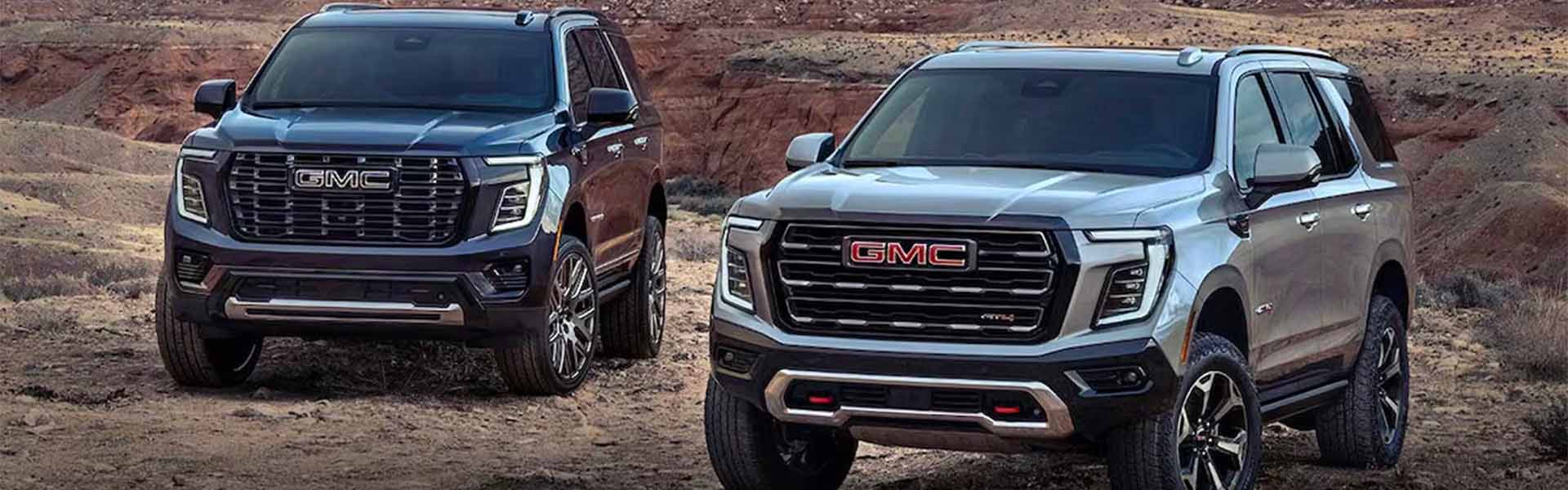 2025 Two rugged GMC Yukon parked in a desert landscape, showcasing bold front grilles, off-road capability, and premium exterior styling.