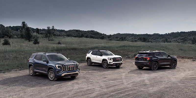 Three SUVs, including a 2026 GMC Terrain AT4, parked on a dirt road surrounded by greenery.